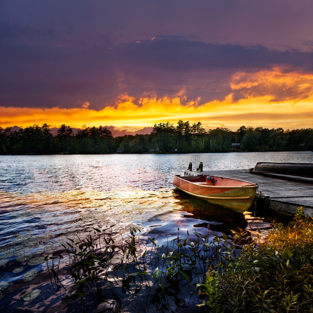 Rowboat tied to dock on beautiful lake with dramatic sunset